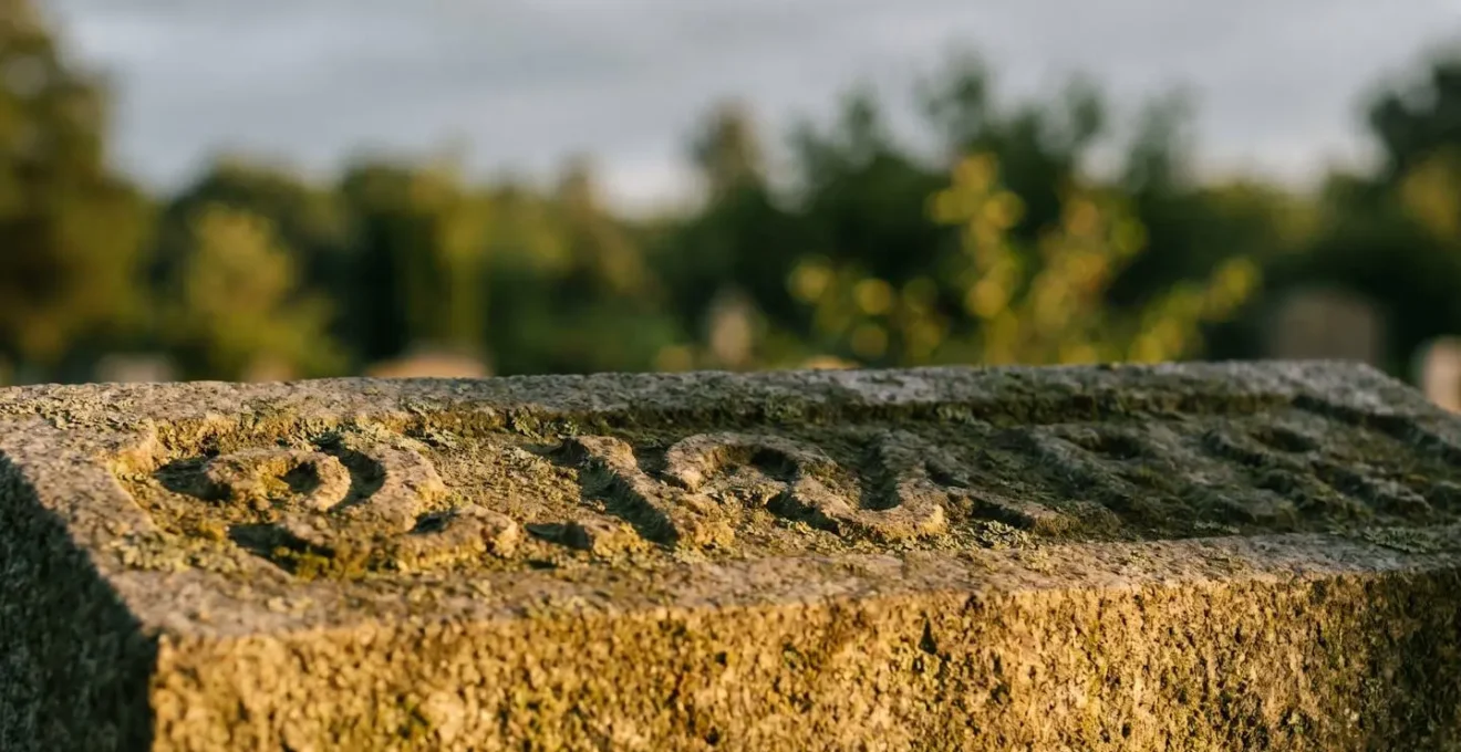 Gros plan d'une inscription gravée sur une pierre tombale en granit, à moitié effacée, éclairée par une lumière rasante qui révèle les lettres invisibles