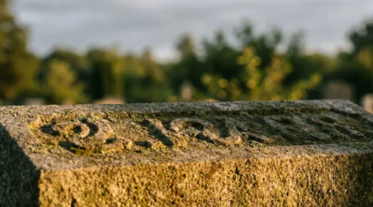 Gros plan d'une inscription gravée sur une pierre tombale en granit, à moitié effacée, éclairée par une lumière rasante qui révèle les lettres invisibles